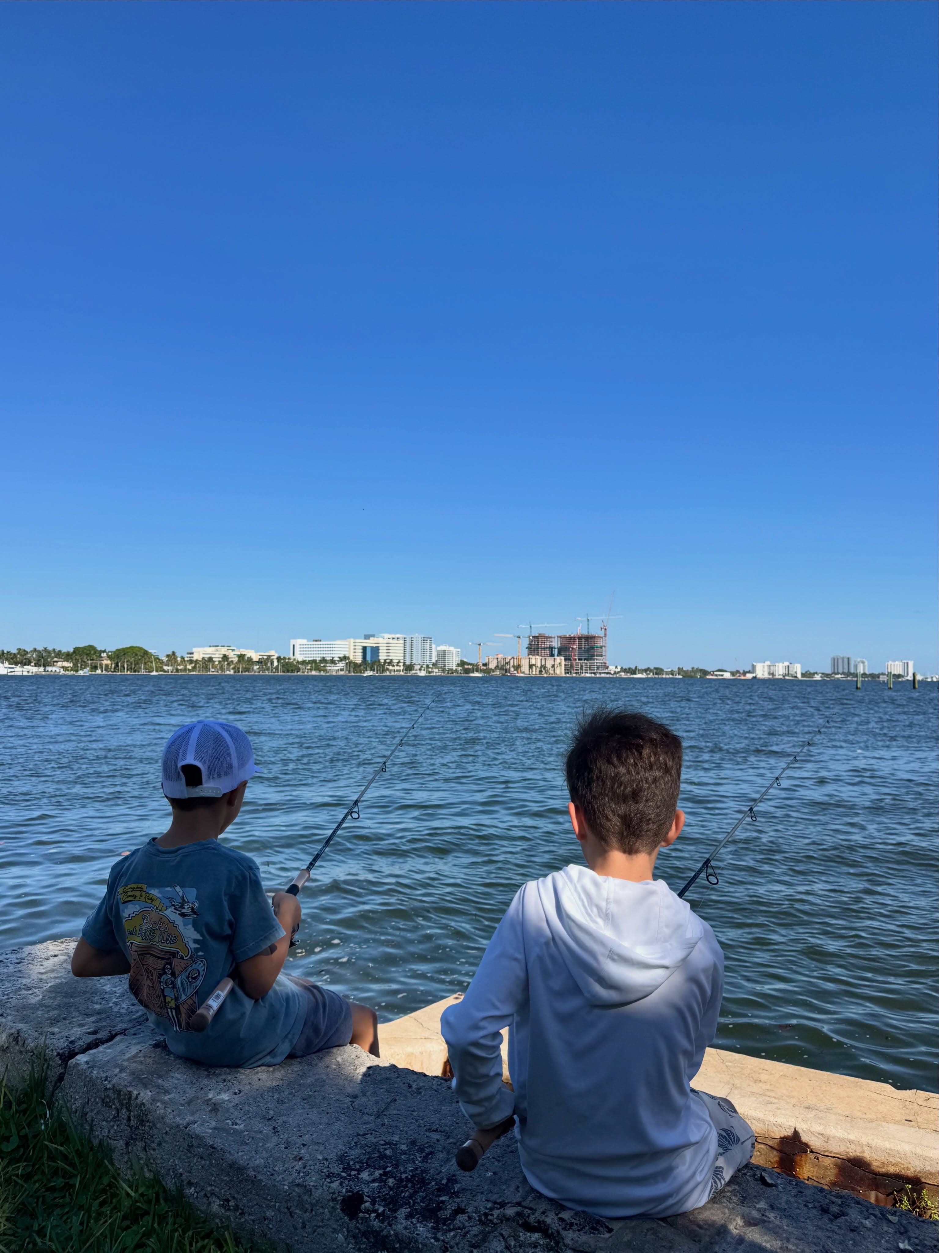 Two boys fishing off the seawall with the city skyline across the water
