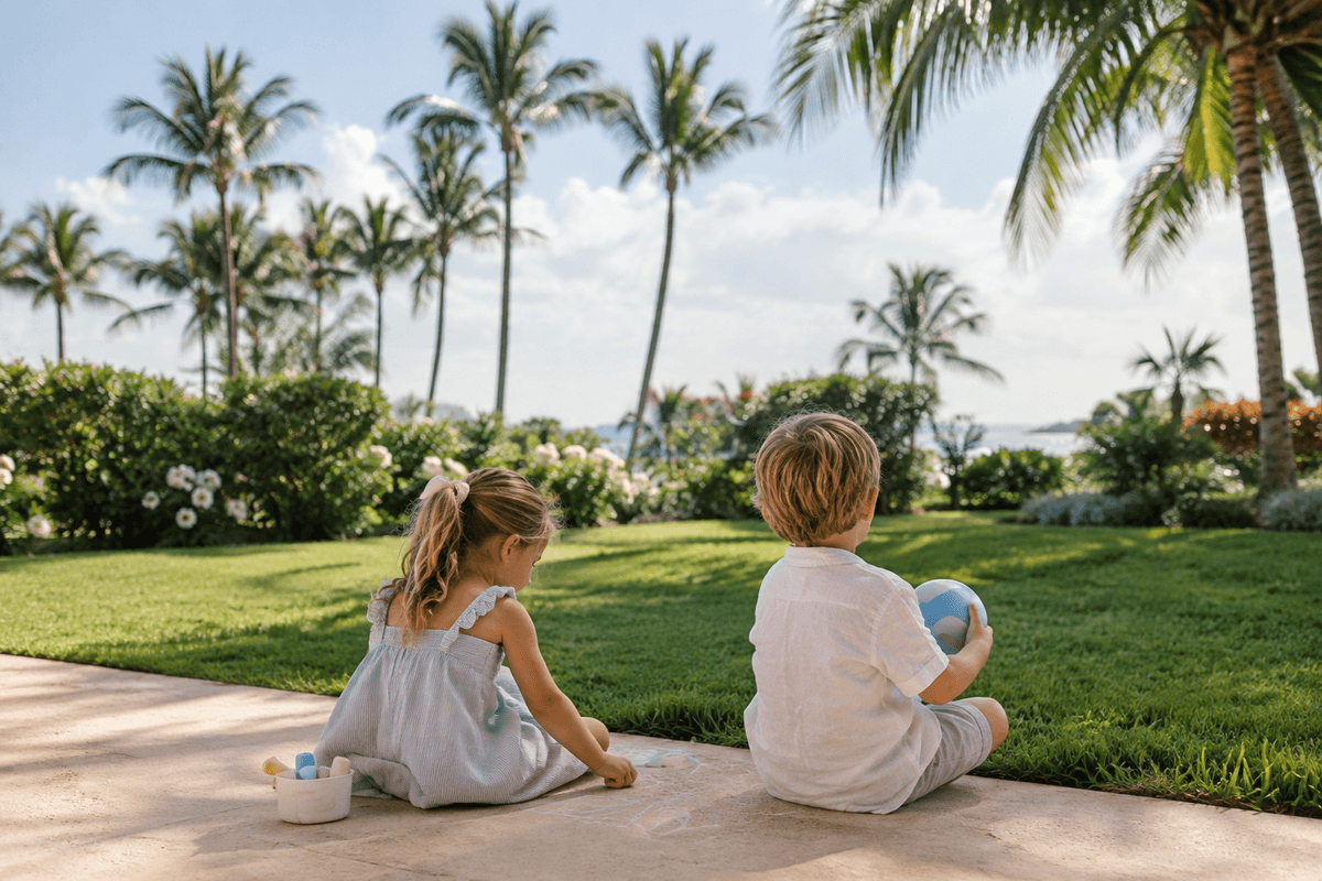 Two kids drawing with chalk on a Palm Beach lawn under palm trees